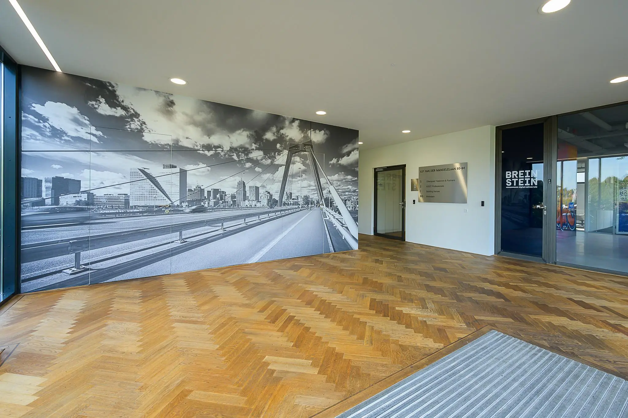 In de entree van een modern kantoorpand aan de K.P. van der Mandelelaan hangt een grote zwart-wit muurfoto van de Erasmusbrug in Rotterdam.